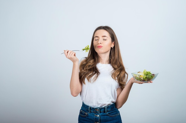 ragazza con una maglietta bianca tiene in mano una ciotola di insalata e mangia