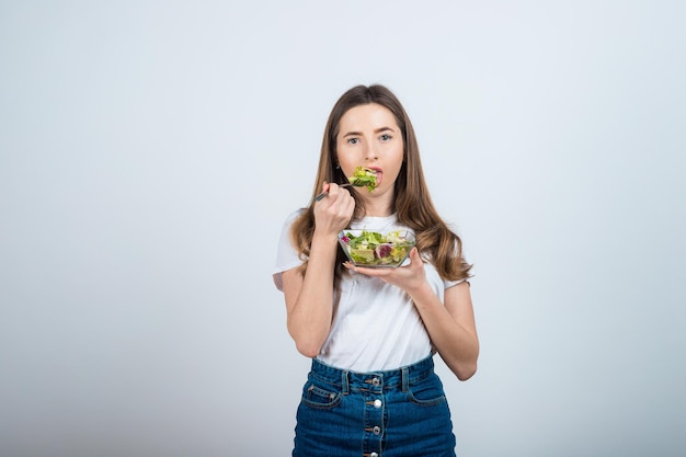 ragazza con una maglietta bianca tiene in mano una ciotola di insalata e mangia