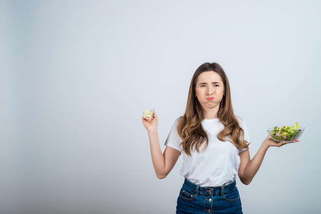 ragazza con una maglietta bianca tiene in mano una ciotola di insalata e mangia