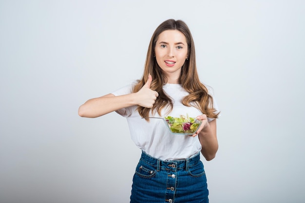 ragazza con una maglietta bianca tiene in mano una ciotola di insalata e mangia