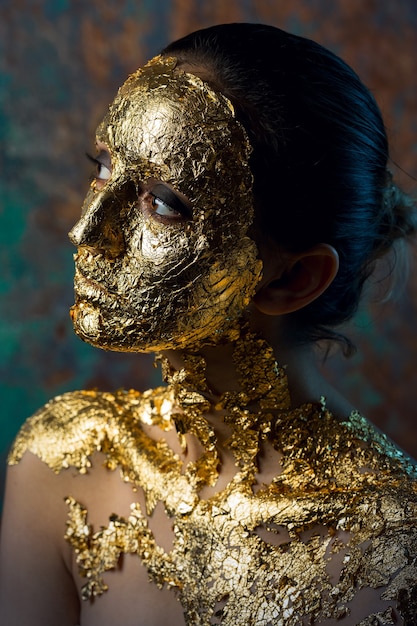 Ragazza con una maschera sul viso fatta di foglia d'oro Cupo ritratto in studio di una bruna su un astratto