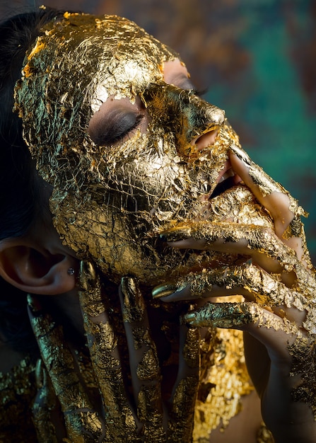 Ragazza con una maschera sul viso fatta di foglia d'oro Cupo ritratto in studio di una bruna su un astratto