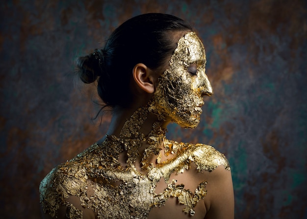 Ragazza con una maschera sul viso fatta di foglia d'oro Cupo ritratto in studio di una bruna