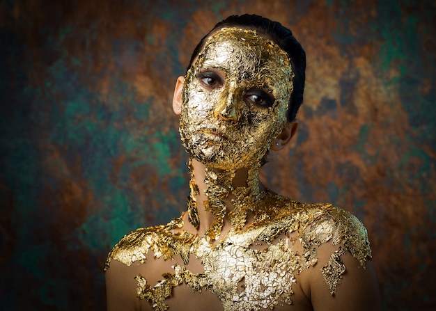 Ragazza con una maschera sul viso fatta di foglia d'oro Cupo ritratto in studio di una bruna