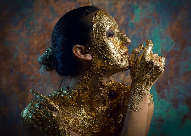 Ragazza con una maschera sul viso fatta di foglia d'oro Cupo ritratto in studio di una bruna