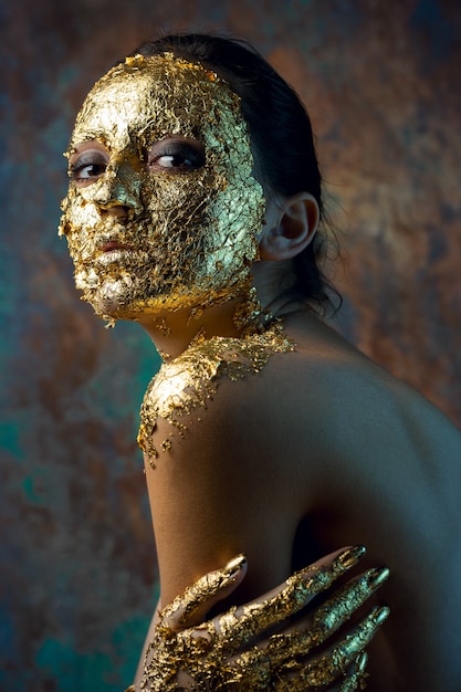 Ragazza con una maschera sul viso fatta di foglia d'oro Cupo ritratto in studio di una bruna