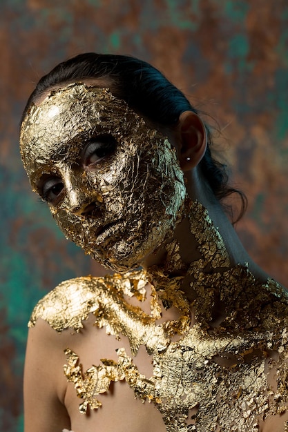 Ragazza con una maschera sul viso fatta di foglia d'oro Ritratto in studio cupo di una bruna su uno sfondo astratto