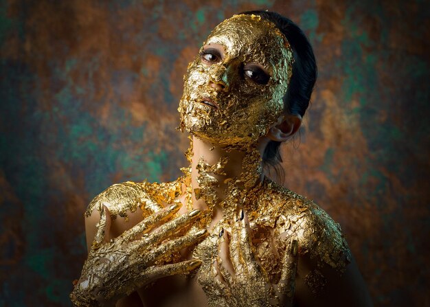 Ragazza con una maschera sul viso fatta di foglia d'oro Ritratto in studio cupo di una bruna su uno sfondo astratto