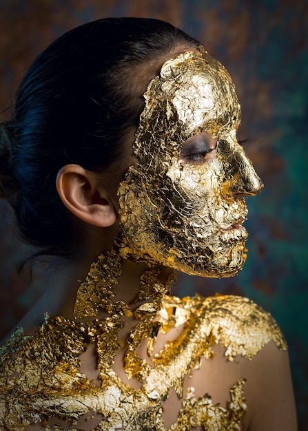 Ragazza con una maschera sul viso fatta di foglia d'oro Ritratto in studio cupo di una bruna su uno sfondo astratto