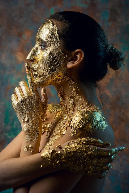 Ragazza con una maschera sul viso fatta di foglia d'oro Ritratto in studio cupo di una bruna su uno sfondo astratto