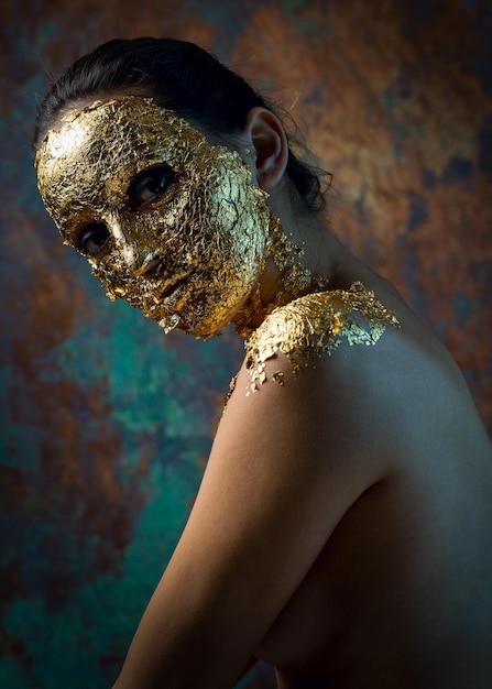 Ragazza con una maschera sul viso fatta di foglia d'oro Ritratto in studio cupo di una bruna su uno sfondo astratto