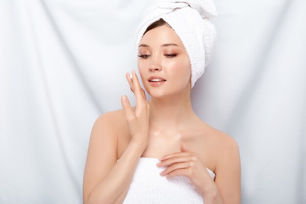 Ragazza con una pelle perfetta in telo da bagno che applica crema per il viso e guardando verso il basso