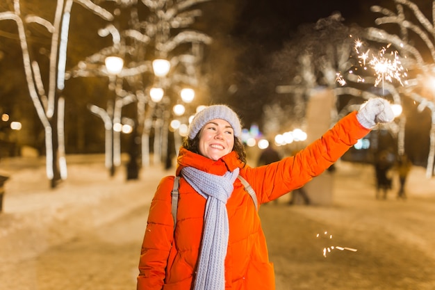 Ragazza con una stella filante in mano all'aperto inverno città sfondo neve fiocchi di neve