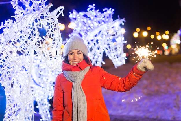 Ragazza con una stella filante in mano all'aperto inverno città sfondo neve fiocchi di neve