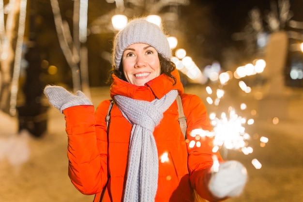 Ragazza con una stella filante in mano all'aperto inverno città sfondo neve fiocchi di neve