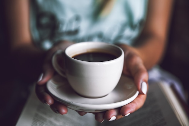 Ragazza con una tazza di caffè e un libro. Sveglia, mattina, pausa, hobby