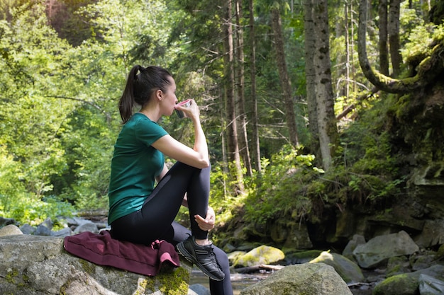 Ragazza con una tazza di tè che si siede su una roccia nella foresta