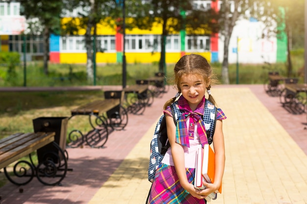 Ragazza con uno zaino e una pila di libri vicino alla scuola. Torna a scuola, il bambino è stanco, libri di testo pesanti. Istruzione, classi scuola primaria, inizio anno scolastico, 1 settembre