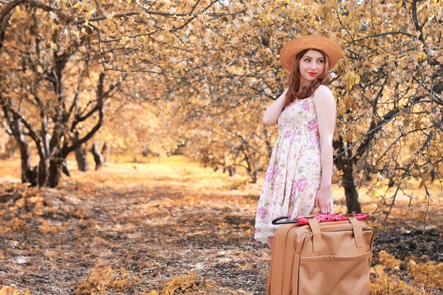 ragazza con valigia in pelle per viaggiare nel parco autunnale a passeggio