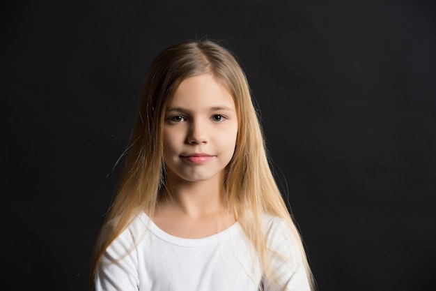 Ragazza con viso adorabile, capelli lunghi e sani, acconciatura su sfondo nero. Concetto di salone di bellezza, copia spazio