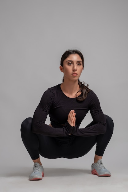 Ragazza concentrata che fa stretching squat sul muro grigio