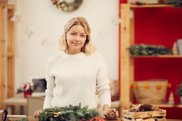 Ragazza contenta in maglione che fa ghirlanda di Natale