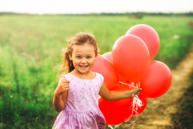 ragazza corre con palloncini rossi in estate in natura