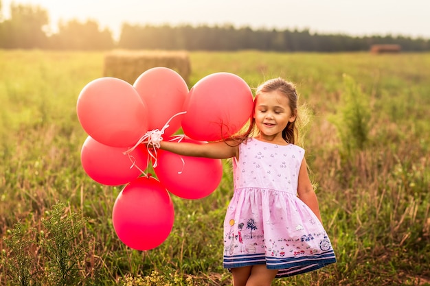 ragazza corre con palloncini rossi in estate in natura