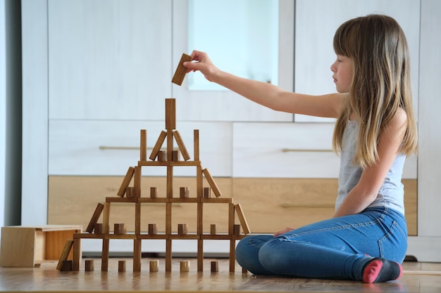 Ragazza creativa del bambino che gioca con il gioco che impila i blocchi giocattolo di legno nell'alta struttura dell'edificio. Concetto di abilità di concentrazione e controllo del movimento della mano