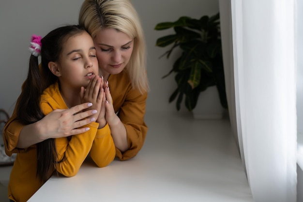 Ragazza cristiana religiosa e sua madre che pregano a casa.
