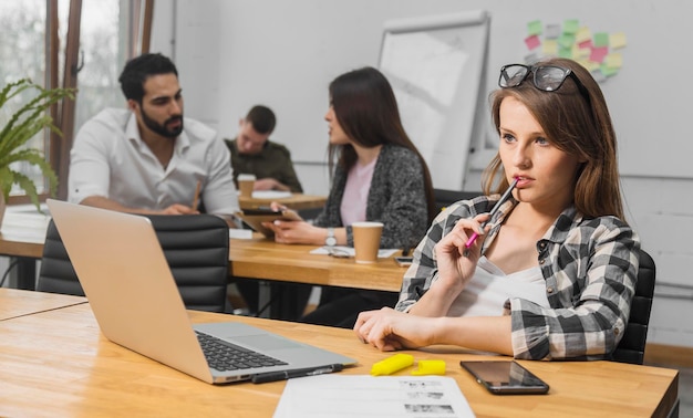 Ragazza dai capelli biondi in camicia casual a quadri che lavora al computer portatile al coperto in un accogliente ufficio bianco