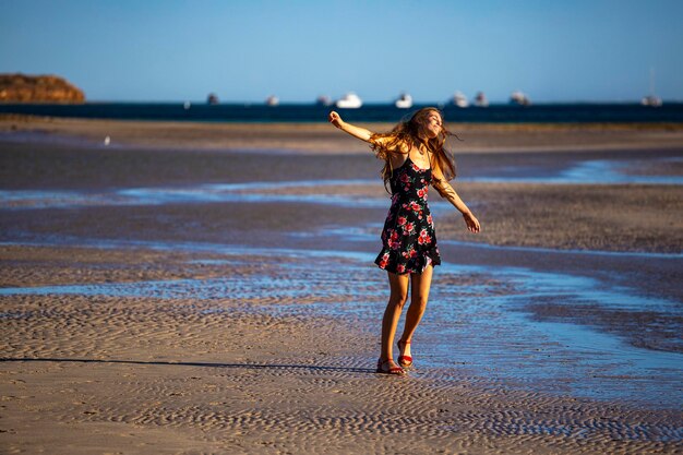 ragazza dai capelli lunghi in abito nero balla sulla spiaggia nella baia di corallo, australia al tramonto, tramonto romantico