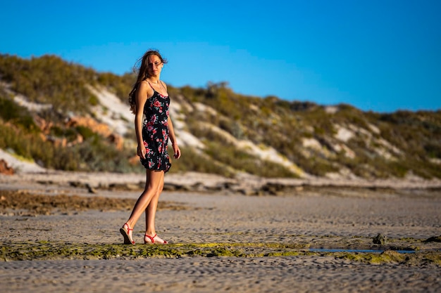 ragazza dai capelli lunghi in abito nero cammina sulla spiaggia di Coral Bay al tramonto, spiaggia dell'Australia occidentale