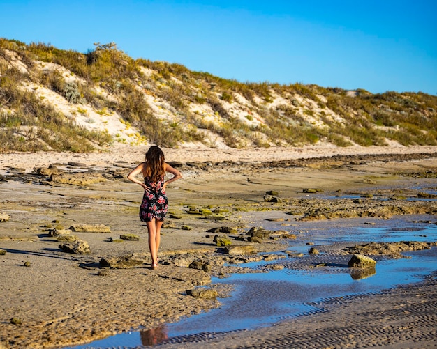 ragazza dai capelli lunghi in abito nero cammina sulla spiaggia di Coral Bay al tramonto, spiaggia dell'Australia occidentale