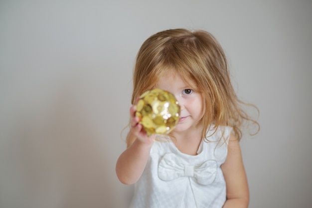 Ragazza dai capelli rossi con ornamento palla d'oro sul muro grigio chiaro