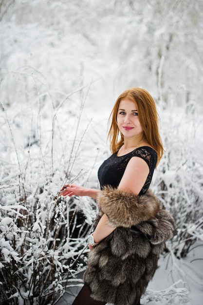 Ragazza dai capelli rossi in pelliccia che cammina al parco innevato d'inverno.