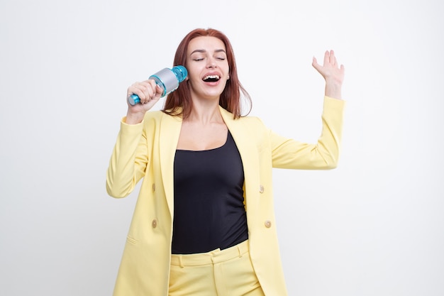 Ragazza dai capelli rossi in un abito giallo canta in un microfono su uno sfondo bianco