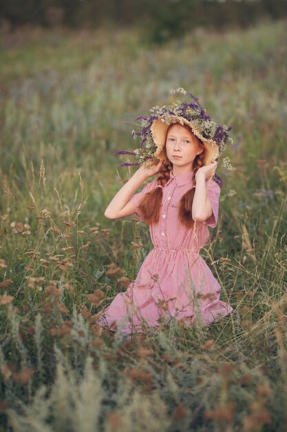 Ragazza dai capelli rossi in un cappello al tramonto su un prato