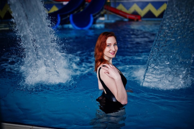 Ragazza dai capelli rossi sexy in costume da bagno nero che riposa nella piscina del parco acquatico