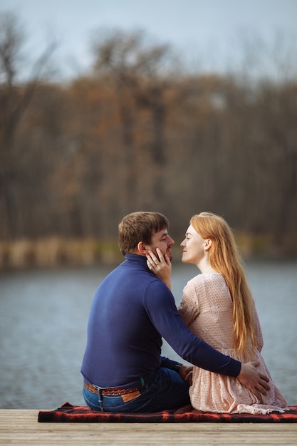 Ragazza dai capelli rossi si siede con un ragazzo in un abbraccio su un molo vicino al lago con una bellissima vista