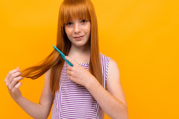 Ragazza dai capelli rossi sorridente che pettina i suoi capelli sopra fondo giallo