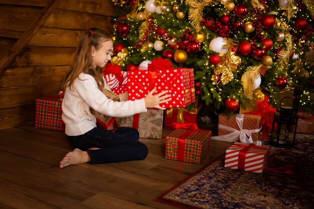 Ragazza davanti all'albero di Natale con scatole regalo decorato soggiorno con camino tradizionale