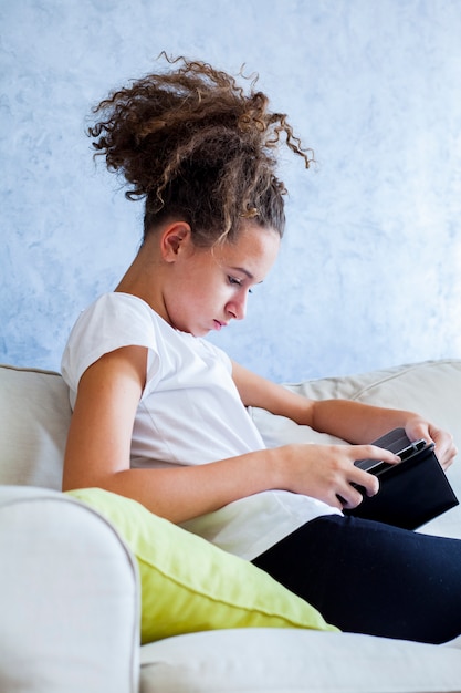 Ragazza dei capelli ricci utilizzando la tavoletta digitale sul divano