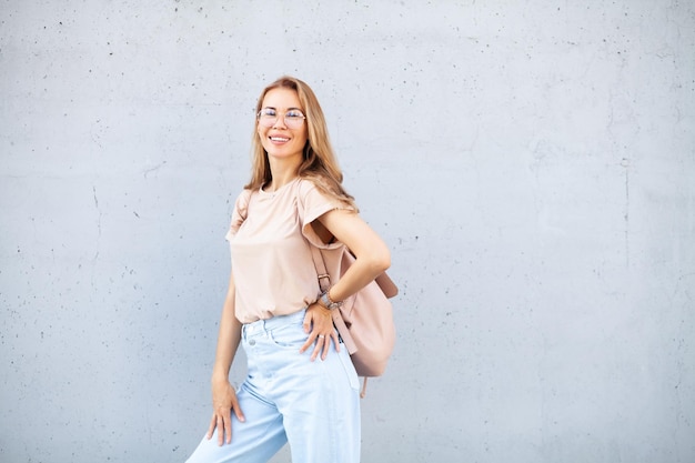 Ragazza dei pantaloni a vita bassa che indossa t-shirt e jeans beige in bianco che posano contro il muro di strada ruvido