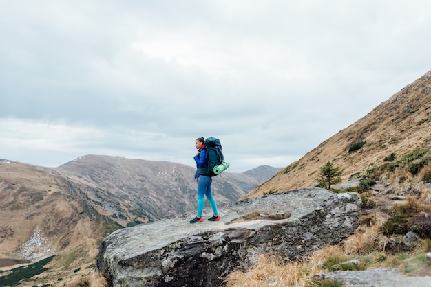 Ragazza dei pantaloni a vita bassa con lo zaino che gode del tramonto sulla cima della montagna nebbiosa