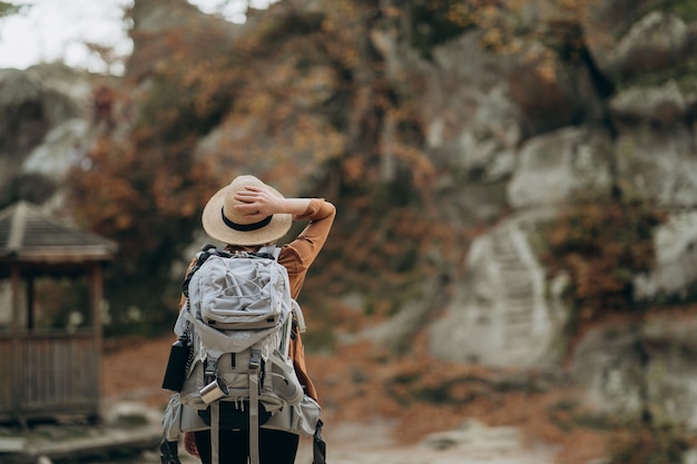 Ragazza dei pantaloni a vita bassa con lo zaino che gode del tramonto sulla montagna di punta