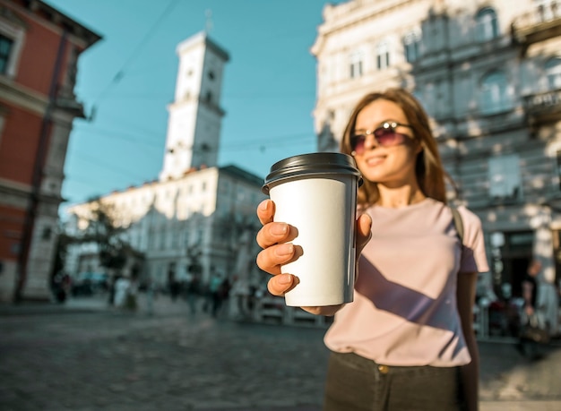 Ragazza dei pantaloni a vita bassa in occhiali da sole che tengono la tazza di caffè