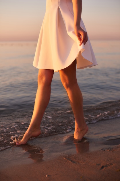 Ragazza dei piedi nudi in vestito bianco nell'acqua ad un ricorso dell'oceano. Vibrazioni mattutine d'estate, camminando sull'acqua