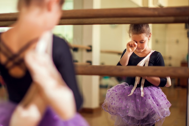 Ragazza del bambino al corso di danza che tiene le scarpe da punta e la colorazione delle lacrime dopo un duro allenamento. Bambini e concetto di sport