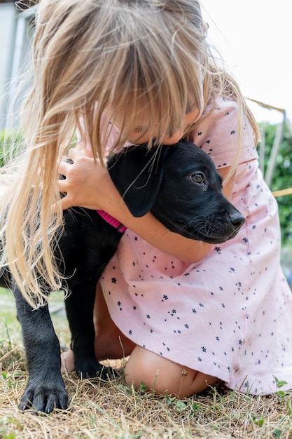 Ragazza del bambino che abbraccia e bacia un cucciolo di labrador retriever balck carino